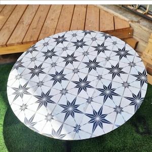 May include: A black round table with a white and black star pattern table cover. The table cover is being placed on the table.