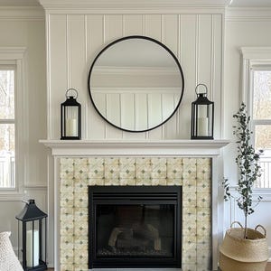May include: A fireplace with a black framed mirror and two black lanterns on the mantel. The fireplace has a black firebox and is decorated with patterned tiles. A small plant in a woven basket sits to the right.
