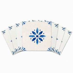 Puede incluir: Un conjunto de baldosas cerámicas cuadradas con un diseño floral. La baldosa central presenta una flor azul con un patrón de puntos, rodeada de baldosas más pequeñas con patrones de hojas en las esquinas. Las baldosas son blancas con detalles azules.