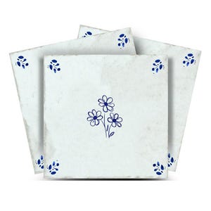 May include: A stack of square, off-white ceramic tiles with a distressed appearance. Each tile features a hand-drawn blue floral design in the centre and smaller floral accents in the corners. The tiles are arranged to show the design.