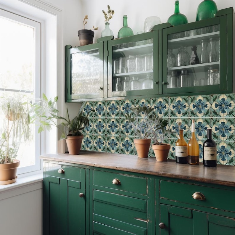 Puede incluir: Armarios de cocina verdes con puertas de vidrio y un salpicadero de azulejos con un patr&oacute;n floral azul y blanco. Los armarios est&aacute;n llenos de cristaler&iacute;a y botellas. Hay plantas en macetas en la encimera.