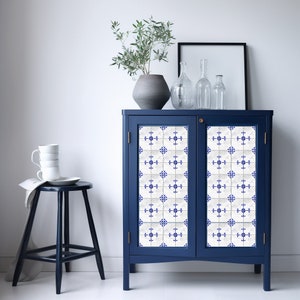 May include: A blue cabinet with two doors, each featuring a white and blue geometric tile pattern. The cabinet is decorated with a vase of green plants and glass bottles.