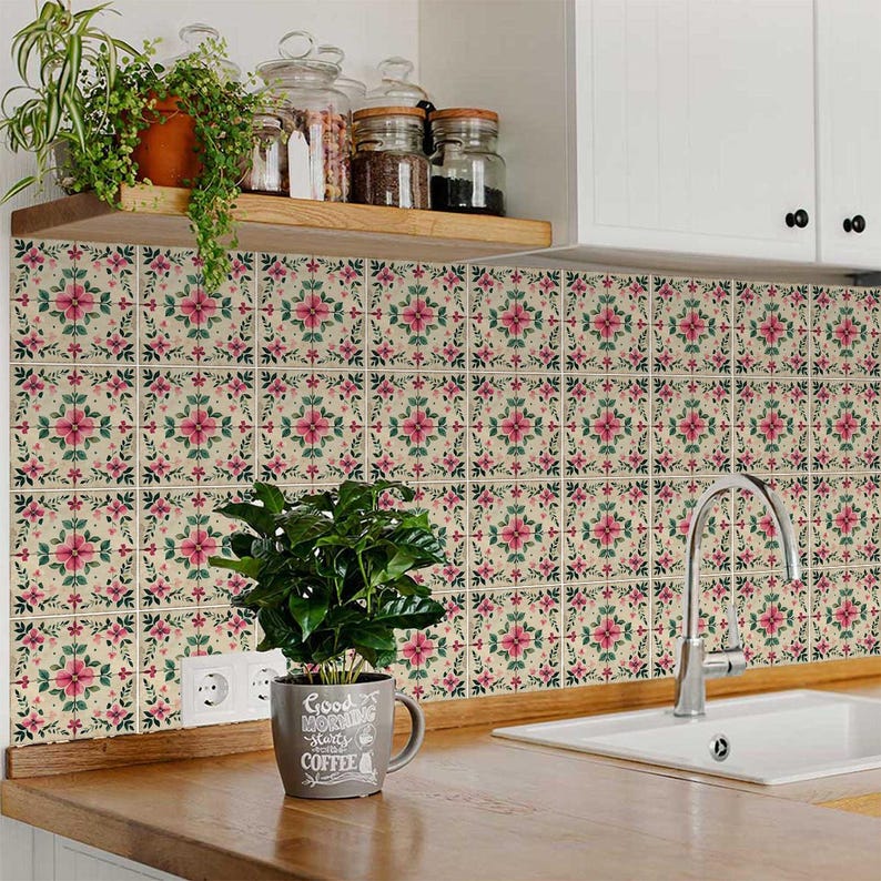 May include: Pink and green floral tile stickers with a white background. The tiles are arranged in a grid pattern and cover a kitchen backsplash. A coffee mug with the text "Good Morning starts with Coffee" is sitting on a countertop in front of the tiles.