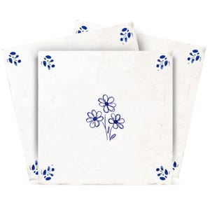 Pode incluir: Três azulejos quadrados brancos dispostos em leque. Cada azulejo apresenta uma ilustração central de linhas azuis de um ramo de três flores e pequenos motivos de folhas azuis posicionados em cada um dos quatro cantos da superfície.