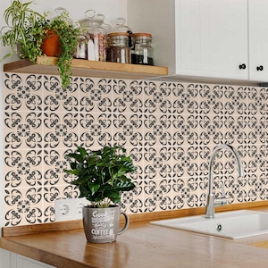 May include: A kitchen backsplash with a beige tile pattern featuring a black floral design. A small potted plant sits on the counter in front of the backsplash. A white ceramic mug with the text "Good Morning starts with Coffee" sits on the counter.
