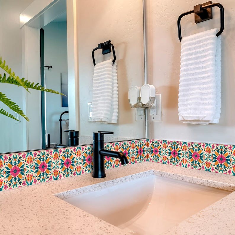 May include: A white bathroom sink with a black faucet and a white countertop. The backsplash is a colorful tile with a floral pattern. There is a white towel hanging on a black towel rack.