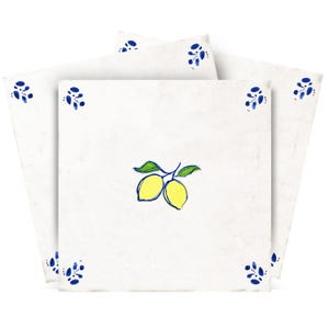 Puede incluir: Azulejos cuadrados blancos con aspecto envejecido, con un diseño de limón dibujado a mano en amarillo y verde. Cada azulejo tiene detalles florales azules en las esquinas. Los azulejos están apilados, mostrando el diseño.