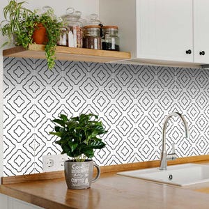 May include: Black and white geometric tile backsplash with a white countertop and a stainless steel faucet. A potted plant with green leaves sits on the countertop. The plant has a mug with the text "Good Morning, starts with coffee" on it.