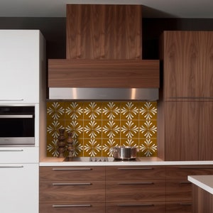 K&ouml;nnte beinhalten: Eine K&uuml;che mit braunen Schr&auml;nken und einer wei&szlig;en Fliesenr&uuml;ckwand mit einem wei&szlig;en Blumenmuster. Die R&uuml;ckwand befindet sich hinter einer Edelstahl-Dunstabzugshaube.