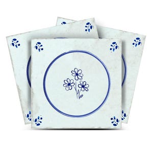 May include: A stack of square ceramic tiles with a white background and blue floral designs. Each tile features a blue circle with a cluster of three flowers in the center. The corners have small blue floral accents.