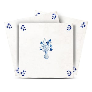 May include: A set of four square, off-white ceramic tiles. Each tile features a blue floral design. One tile has a vase of flowers, and the others have corner floral accents. The tiles are arranged in a fan shape.