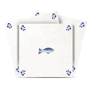 Pode incluir: Azulejos de cerâmica brancos com uma ilustração de peixe azul no centro. Cada azulejo tem desenhos florais azuis nos cantos. Os azulejos estão dispostos em forma de leque.