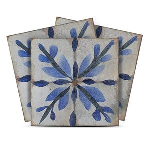 Puede incluir: Tres azulejos de cerámica azul y blanco con un diseño floral. Los azulejos tienen un aspecto desgastado y son perfectos para añadir un toque de encanto rústico a cualquier espacio.