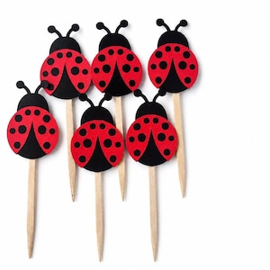 May include: Six ladybug-shaped cupcake toppers. Each topper features a red body with black spots and a black head with antennae. The ladybugs are attached to wooden sticks, perfect for decorating baked goods.