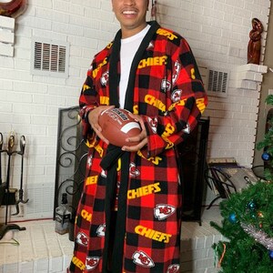 May include: A red and black flannel robe with the Kansas City Chiefs logo and the word "Chiefs" repeated throughout. The robe has a black sash and is being worn by a person holding a football.
