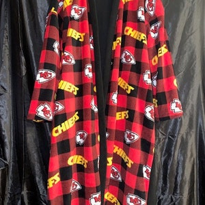 May include: A red and black fleece robe with a chequered pattern and the word "Chiefs" repeated throughout. The robe has a black inner lining and a shawl collar.