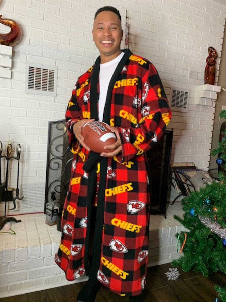 May include: A red and black flannel robe with the Kansas City Chiefs logo and the word "Chiefs" repeated throughout. The robe has a black sash and is being worn by a person holding a football.