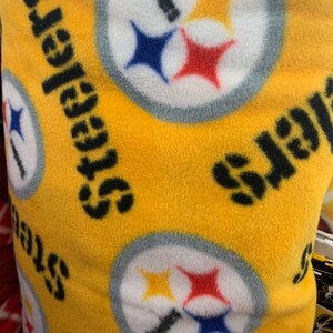 May include: Yellow fabric with a repeating pattern of the Pittsburgh Steelers logo. The logo is white with black and yellow stars, a black stripe, and a blue and red star.