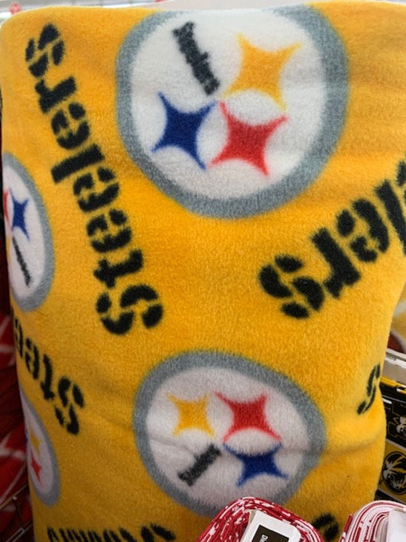 May include: Yellow fabric with a repeating pattern of the Pittsburgh Steelers logo. The logo is white with black and yellow stars, a black stripe, and a blue and red star.