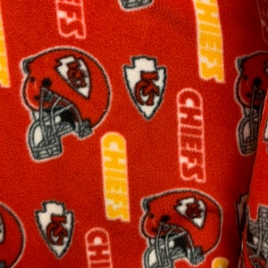 May include: Red fleece fabric with a repeating pattern of a football helmet, a stylised arrow with the letters "KC" and the word "Chiefs" in yellow.