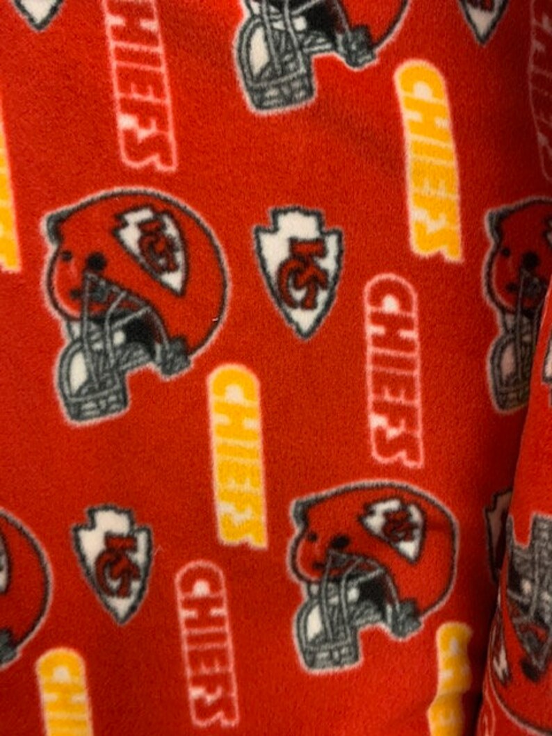 May include: Red fleece fabric with a repeating pattern of a football helmet, a stylised arrow with the letters "KC" and the word "Chiefs" in yellow.