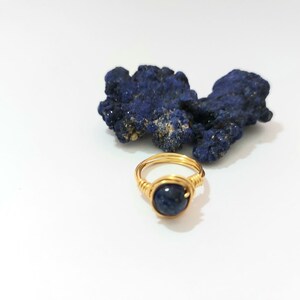 K&ouml;nnte beinhalten: Ein goldfarbener Ring, der mit Draht umwickelt ist und einen dunkelblauen Edelstein tr&auml;gt. Der Ring liegt auf einer wei&szlig;en Oberfl&auml;che neben einem St&uuml;ck blauen Azurite.