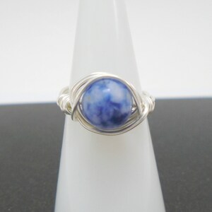 May include: A silver wire wrapped ring with a blue and white gemstone.