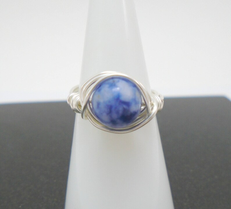 May include: A silver wire wrapped ring with a blue and white gemstone.