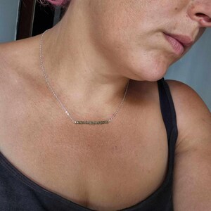 May include: A silver chain necklace with a bar pendant made of small green stones.