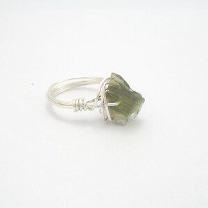 May include: A silver wire wrapped ring with a green gemstone. The gemstone is a rough, irregular shape.