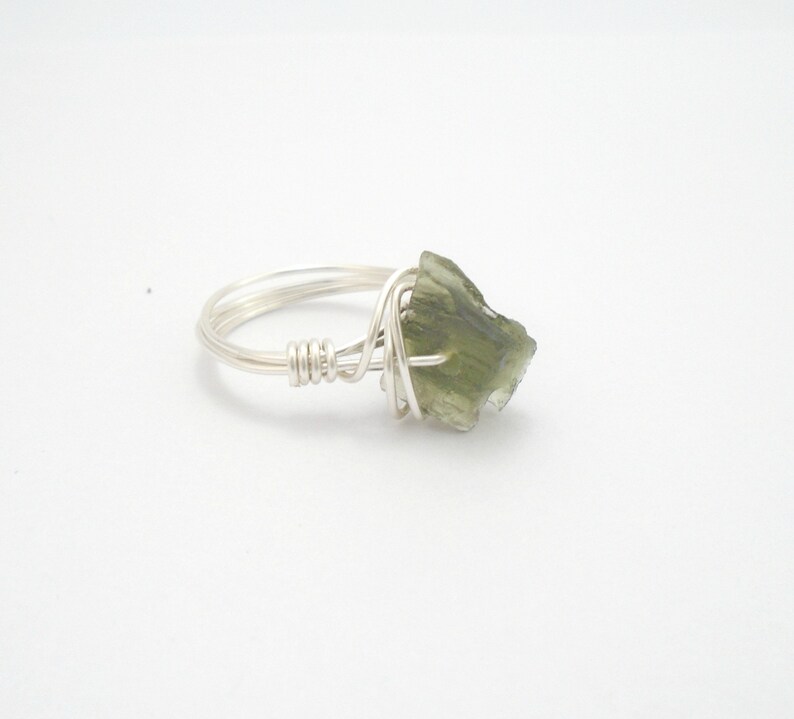 May include: A silver wire wrapped ring with a green gemstone. The gemstone is a rough, irregular shape.