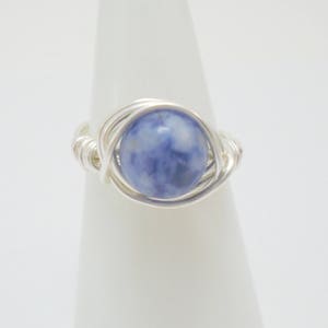 May include: A silver wire wrapped ring with a blue and white gemstone.