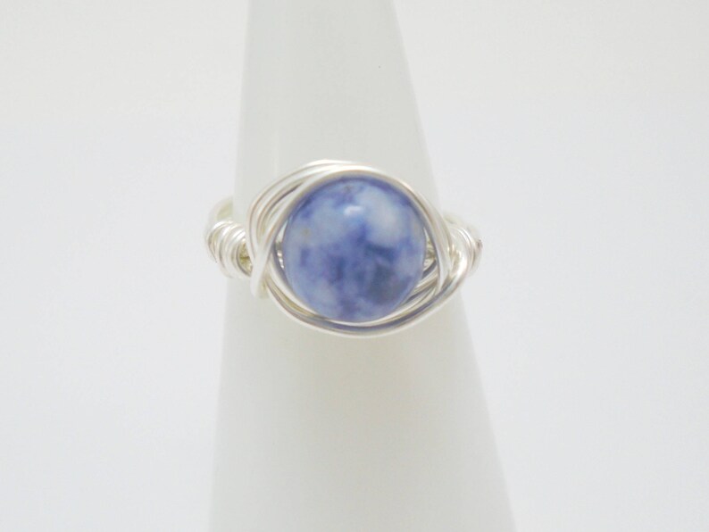 May include: A silver wire wrapped ring with a blue and white gemstone.