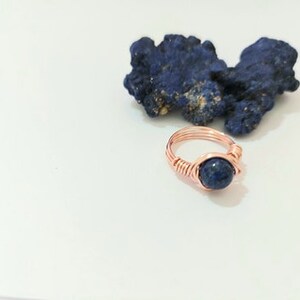 K&ouml;nnte beinhalten: Ein Ring aus Kupferdraht mit einem dunkelblauen Edelstein. Der Ring ist mit Kupferdraht umwickelt und hat ein schlichtes Design.