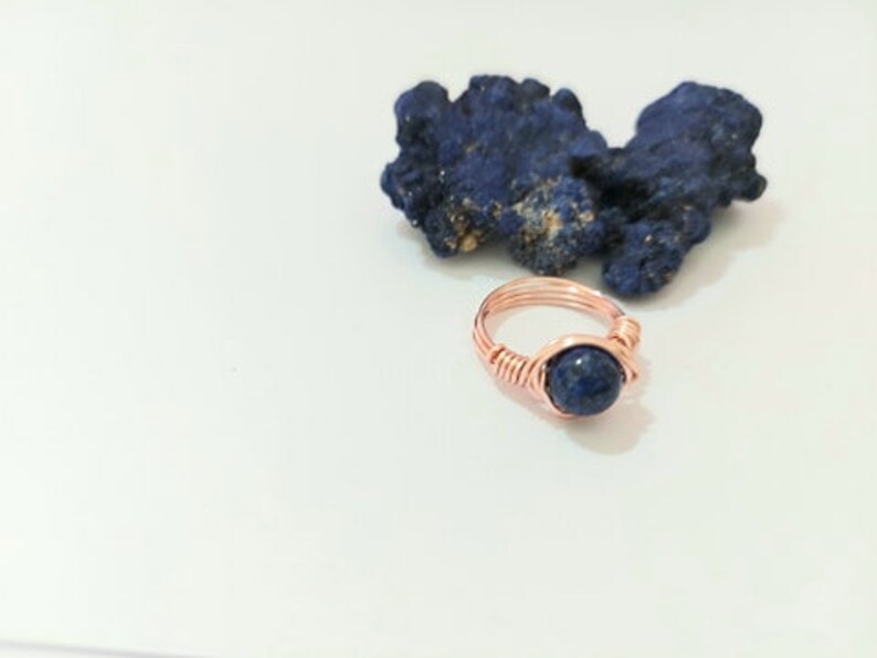 K&ouml;nnte beinhalten: Ein Ring aus Kupferdraht mit einem dunkelblauen Edelstein. Der Ring ist mit Kupferdraht umwickelt und hat ein schlichtes Design.