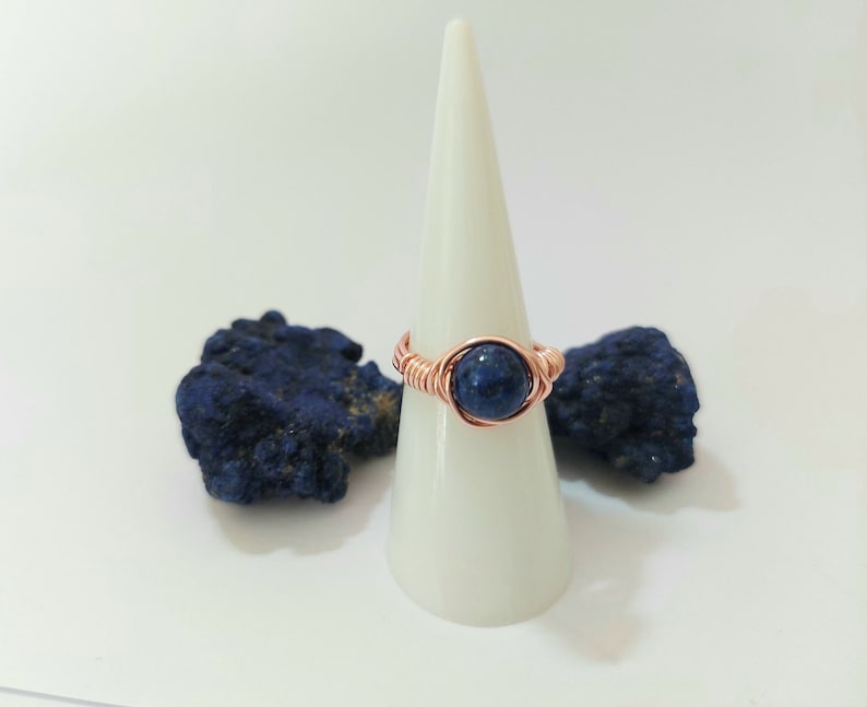K&ouml;nnte beinhalten: Ein Ring aus Kupferdraht mit einem dunkelblauen Edelstein. Der Ring wird auf einem wei&szlig;en Kegel pr&auml;sentiert.