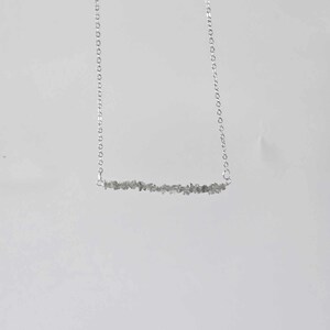 May include: A silver chain necklace with a bar pendant made of small, grey stones.