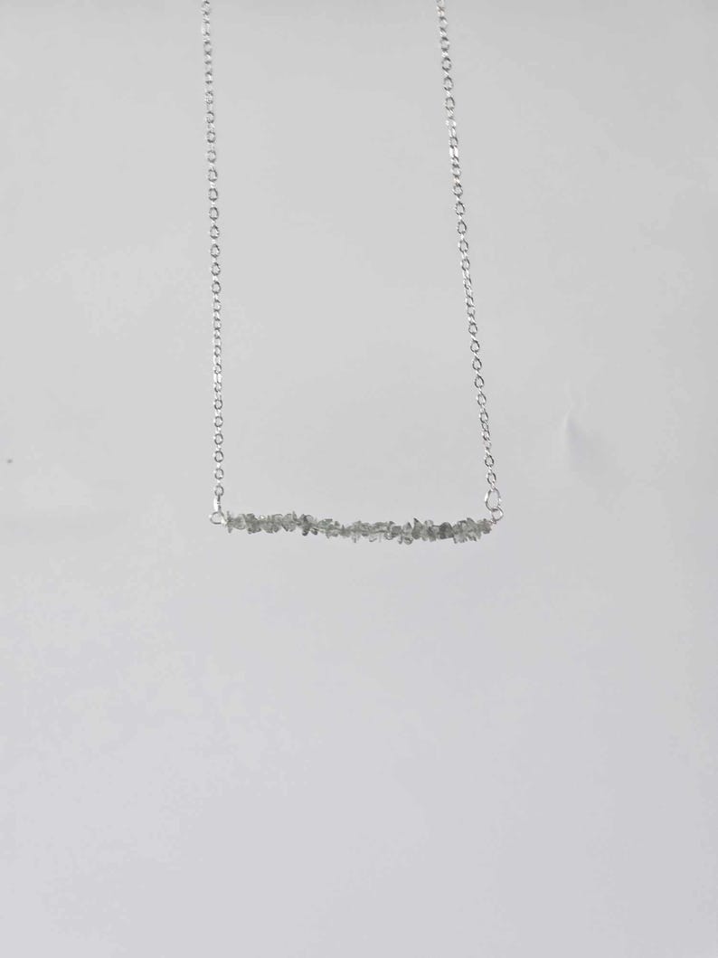 May include: A silver chain necklace with a bar pendant made of small, grey stones.