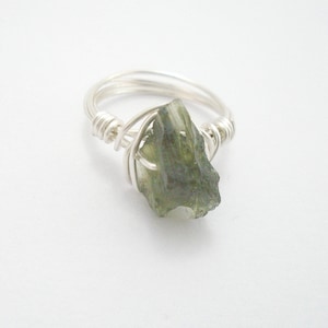 May include: A silver wire wrapped ring with a green gemstone. The gemstone is a rough, irregular shape.