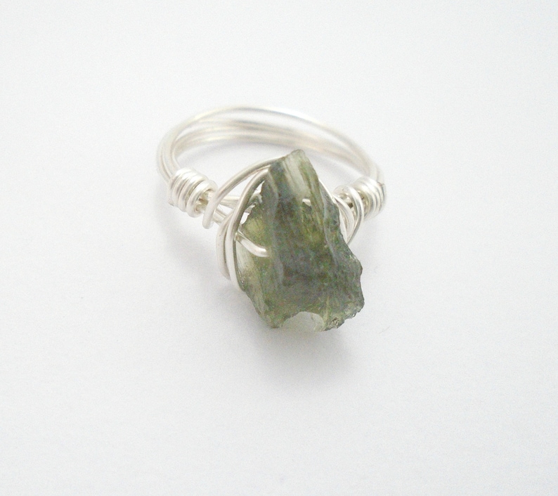 May include: A silver wire wrapped ring with a green gemstone. The gemstone is a rough, irregular shape.