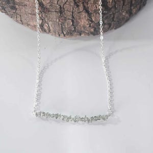 May include: A silver chain necklace with a delicate bar of small, light green stones.