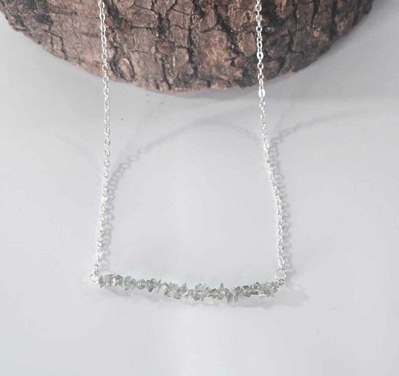 May include: A silver chain necklace with a delicate bar of small, light green stones.