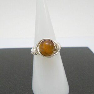 May include: A silver wire wrapped ring with a round, brown tiger's eye gemstone.
