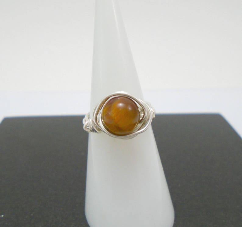 May include: A silver wire wrapped ring with a round, brown tiger's eye gemstone.
