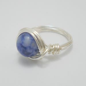 May include: A silver wire wrapped ring with a blue and white gemstone.
