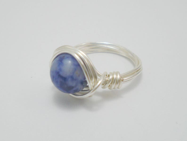 May include: A silver wire wrapped ring with a blue and white gemstone.