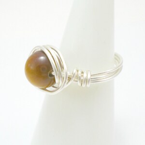 May include: A silver wire wrapped ring with a brown tiger's eye stone.