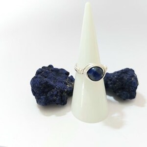 K&ouml;nnte beinhalten: Ein Ring aus Silberdraht mit einem blauen Edelstein. Der Ring wird auf einem wei&szlig;en Kegel pr&auml;sentiert.