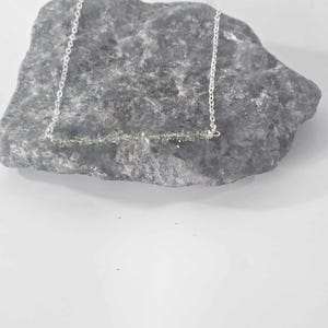 May include: A silver chain necklace with a bar pendant made of small, light green gemstones.