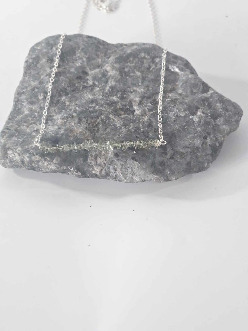 May include: A silver chain necklace with a bar pendant made of small, light green gemstones.